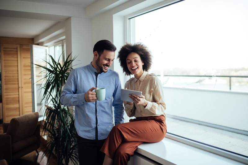 Couple at home by the window, researching on a smartphone and discussing whether they should pay mortgage points.