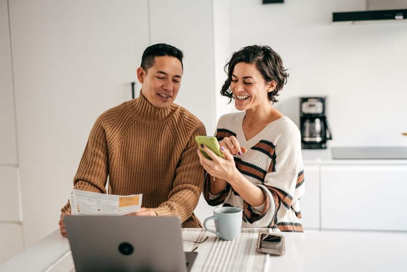 Couple laughs while looking at phone, computer.