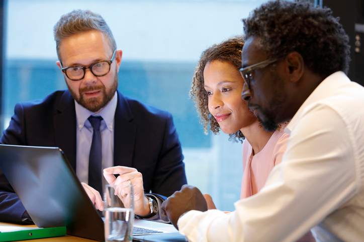 A couple buying a house with no credit looks on at a mortgage lender sitting at a computer.