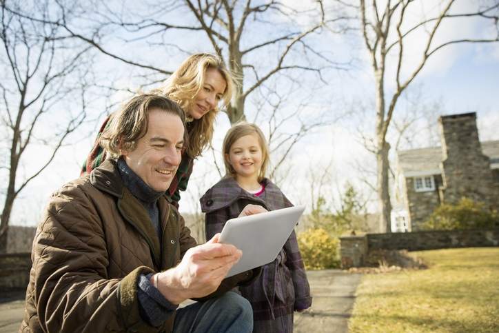 A family consults a tablet computer on a large property with a home