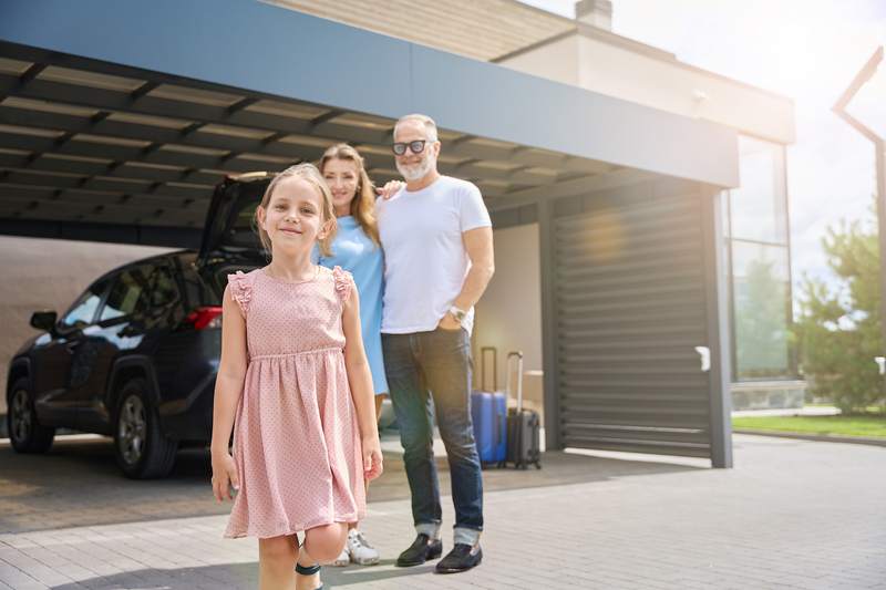 A girl and her parents stand in the driveway of a luxury home.