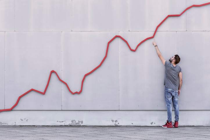 A man stands and points at an ascending red line on a wall.