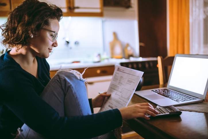 Woman calculates refinance closing costs at kitchen table